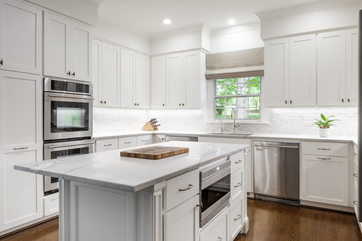 Spacious white kitchen with marble island and stainless steel double oven in Wolfe Homes Greensboro remodel