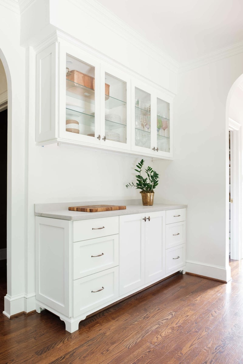 White cabinet area with glass-paneled storage and wooden countertop in Greensboro remodel by Wolfe Homes